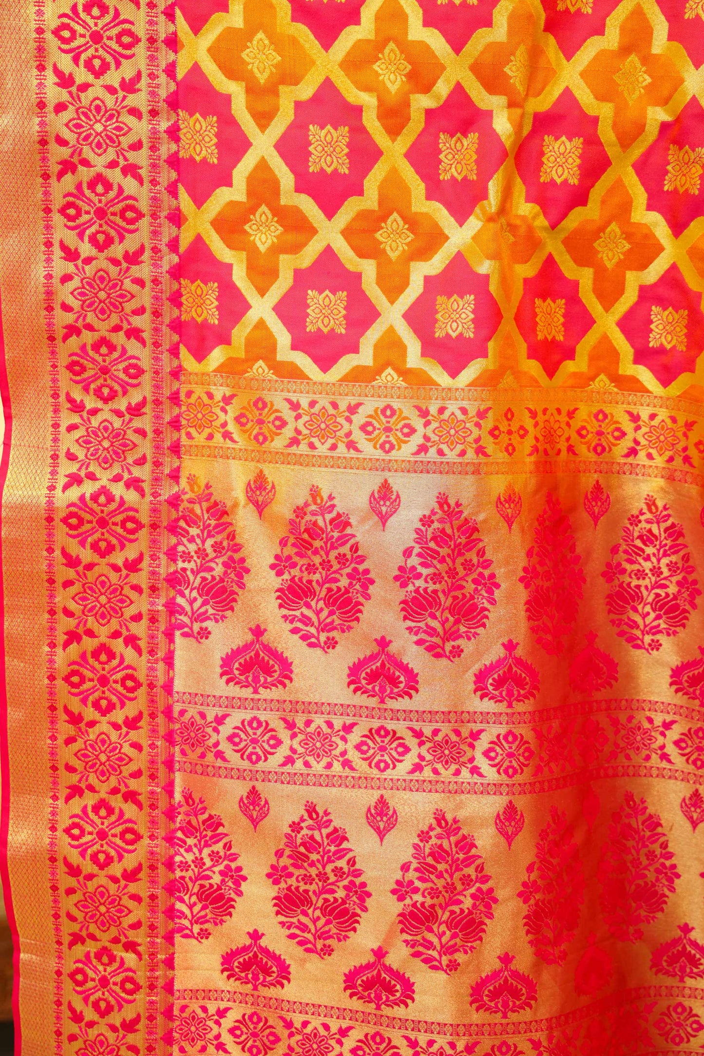 Close up view of Handloom pink Banarasi saree with gold zari motifs and bright yellow border, traditional festive wear.